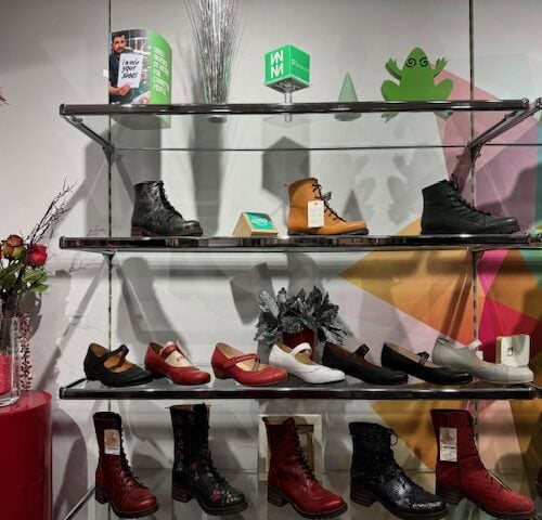 Schuhgeschäftauslage mit bunten Stiefeln und Schuhen, buntem Hintergrund und Weihnachtsdekoration.