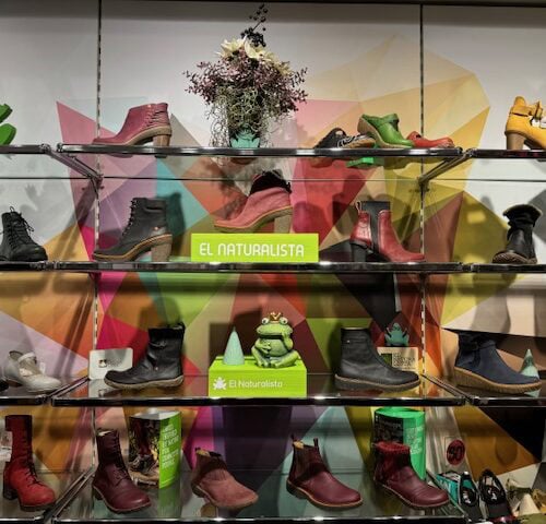 Schuhgeschäft-Display mit bunten Stiefeln, grünen Dekorationselementen und Pflanzen.