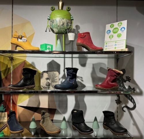 Schuhladen mit verschiedenen bunten Schuhen; Froschfigur und Deko im Hintergrund.