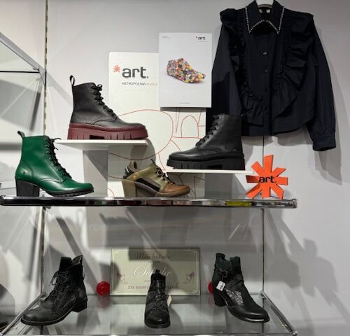 Regalbrett mit verschiedenen Schuhen und einer schwarzen Bluse als Auslage in einem Laden.