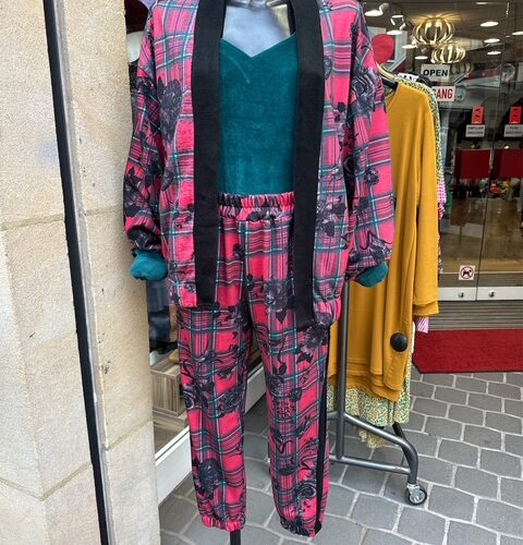 Schaufensterpuppe in roter, karierter Kleidung mit schwarzem Muster und grünem Oberteil.