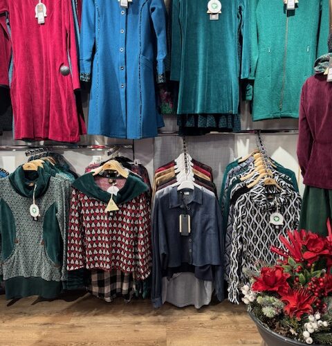 Bunte Damenoberbekleidung in Rot, Blau und Grün, in einem Bekleidungsgeschäft auf Holzboden.