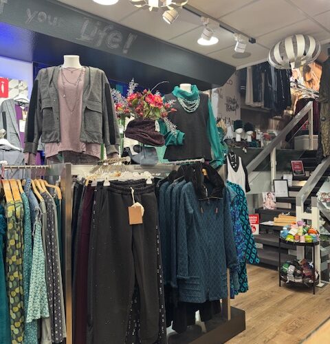 Ein Boutique-Schaufenster mit Herbstkleidung in gedeckten Farben, vielseitige Stoffe, Holzboden.