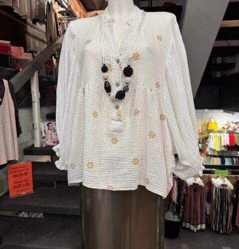 Schaufensterpuppe mit weißer Bluse und schwarzer Halskette, in einem Geschäft mit Kleidung.