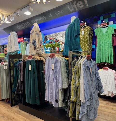 Kleiderladen mit bunten Kleidern auf Ständern und leuchtend blauer Hintergrundbeleuchtung.