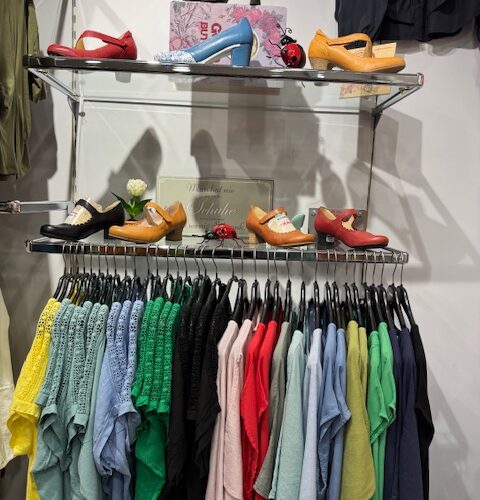 Ein Regal mit bunten Schuhen und darunter hängende farbige T-Shirts.