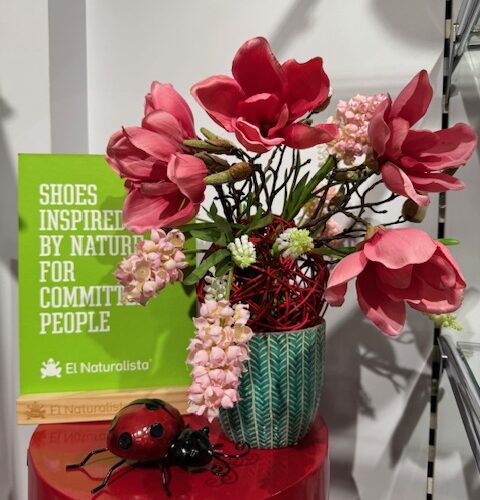Blumen in roter Vase auf rotem Tisch, Schild mit Text im Hintergrund, grüne Karte.