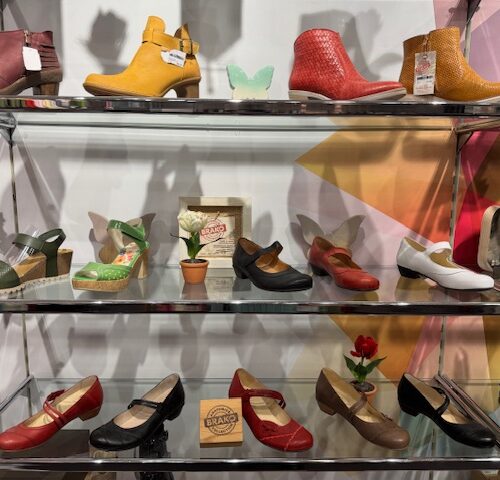 Verschiedene bunte Schuhe auf Glasregalen in einem Geschäft vor einer farbenfrohen Wand.