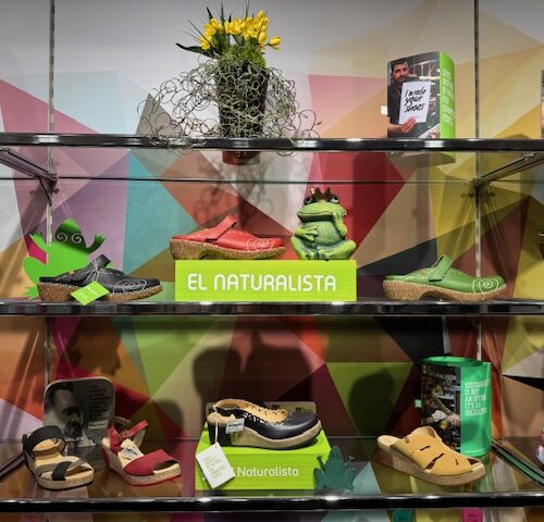 Schaufenster mit bunten El Naturalista-Schuhen und Pflanzen auf mehrfarbigem Hintergrund.