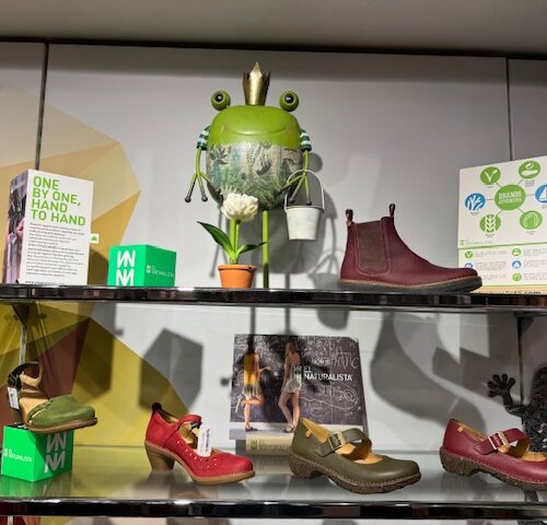 Regal aus Metall mit bunten Schuhen, Frosch-Deko und grünen, geometrischen Mustern im Laden.