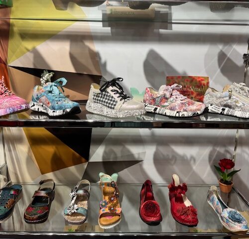 Bunte, dekorative Schuhe auf Regal ausgestellt, darunter Sandalen und Sneakers in leuchtenden Farben.