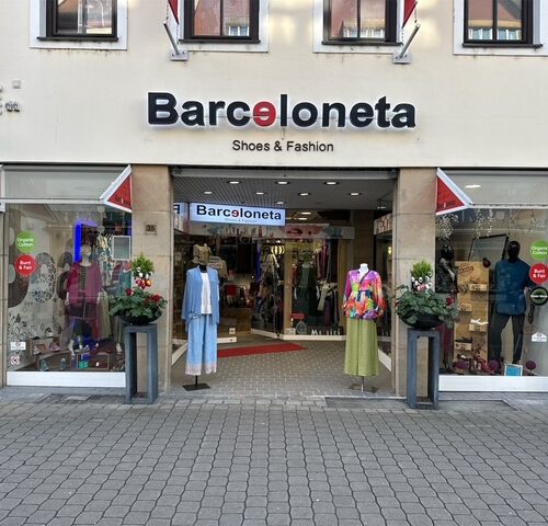 Eingang eines Modegeschäfts mit Schaufensterpuppen in bunten Kleidern, Geschäfteingang mit Schild.