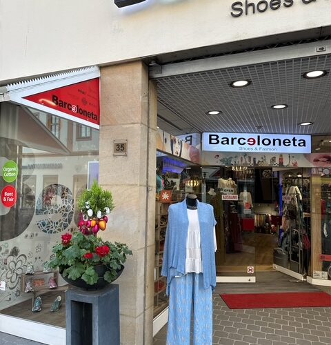 Schaufenster mit blauem Kleid, blauem Schal, Blumen rechts; Barceloneta-Geschäft im Hintergrund.